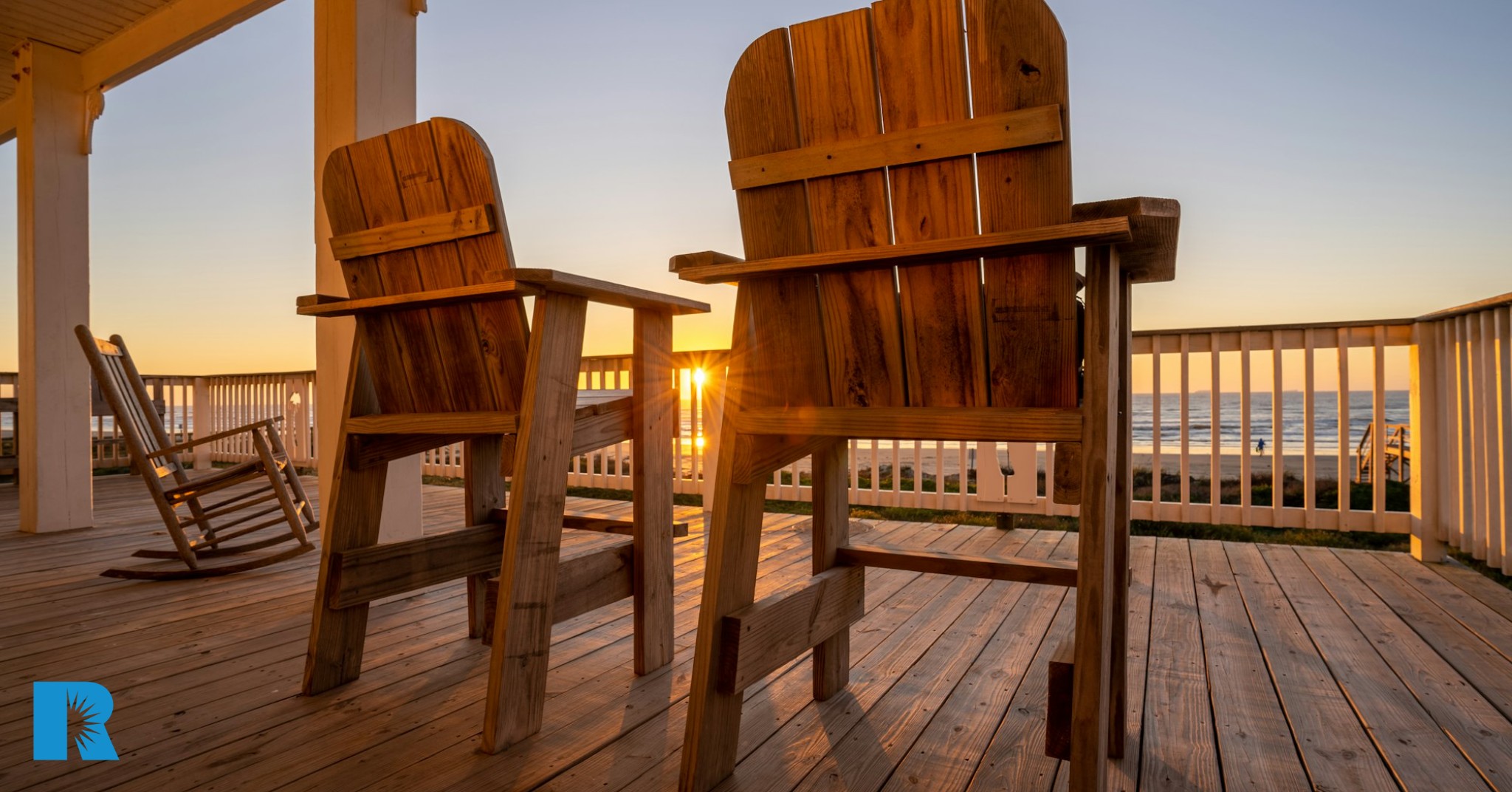 A pair of rocking chairs rest on a front porch as the sun sets.