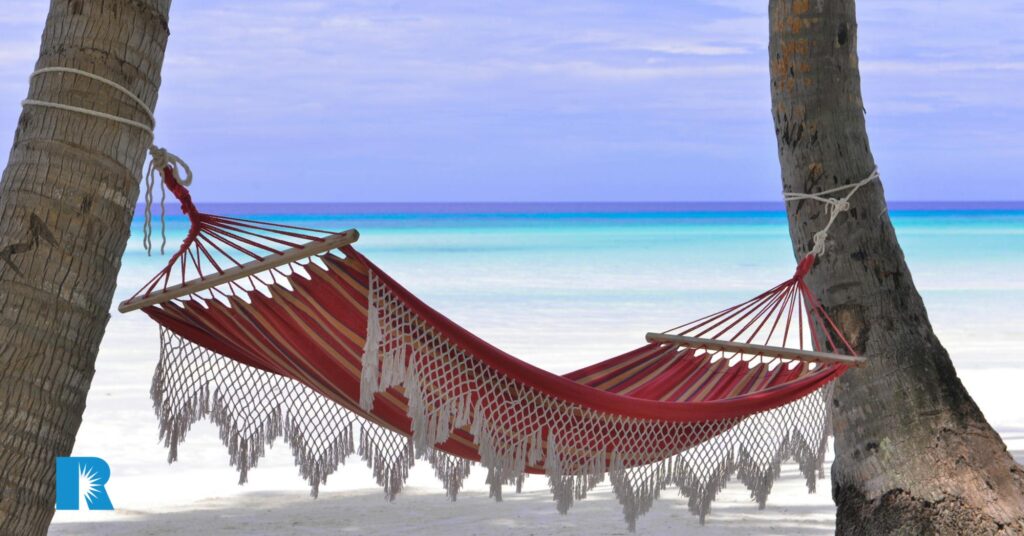 Photo of a hammock stretched between two palm trees on a tropical beach.